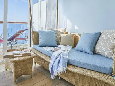 Verandakabine Deluxe Lounge an Bord der AIDAcosma: Rattan-Sitzbank mit Kissen, Beistelltisch. Balkon mit Liege und Meerblick.