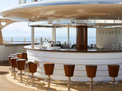 Die Ocean Bar auf dem Sonnendeck der AIDAcosma, mit einer Theke, Barhockern und Meerblick im Hintergrund an einem sonnigen Tag.