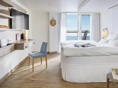 Eine helle und modern gestaltete Balkonkabine der AIDAcosma. Zu sehen sind ein grosses Bett, ein Schreibtisch mit TV und ein Balkon mit Meerblick.
