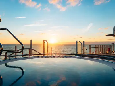 Ein Whirlpool auf dem Oberdeck der AIDAcosma reflektiert den Himmel. Im Hintergrund versinkt die Sonne golden über dem weiten Meer und taucht die Szene in warmes Licht.