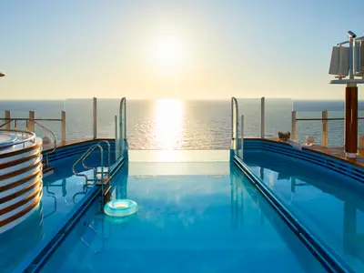Der Infinity-Pool an Bord der AIDAcosma spiegelt den sonnigen Himmel und das Meer wider. Ein blauer Rettungsring schwimmt im Vordergrund.