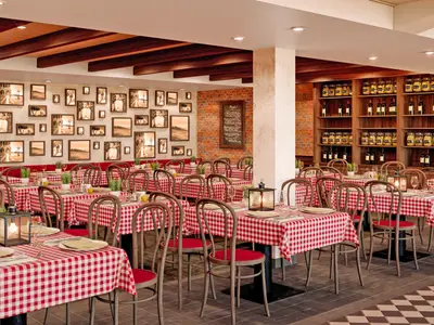 Das Ristorante Mamma Mia an Bord der AIDAcosma. Ein grosser Speisesaal mit rot-weiss karierten Tischdecken und Holzstühlen. Wände sind mit Bildern und Ziegeln dekoriert, dazu Regale mit Wein und Pasta.