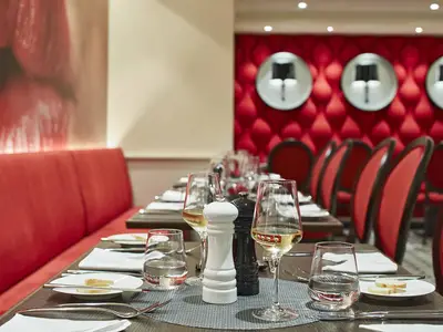 Das elegante Restaurant 'French Kiss' an Bord der AIDAcosma zeigt eine rote, gepolsterte Einrichtung. Gedeckte Tische mit Gläsern und Besteck warten auf Gäste. Ohne Personen.