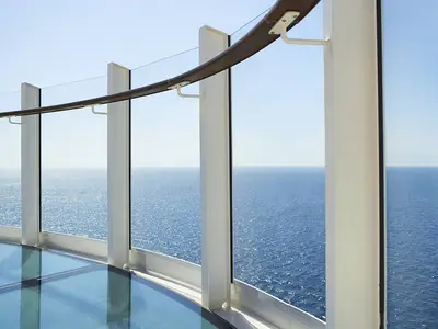 Panoramablick vom Skywalk der AIDAcosma mit transparenter Glasbrüstung und Holztraversen. Das tiefe Blau des Meeres trifft auf den hellblauen Himmel.