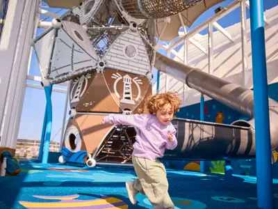 Ein fröhliches Kind spielt im FUNPARK an Bord der AIDAdiva. Eine große Kletterstruktur mit Leuchtturmmotiv und eine Rutsche prägen den blauen Spielplatz.