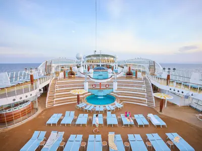 Weitläufiges Pooldeck an Bord der AIDAdiva mit blauen Pools, Wasserfällen und Terrassen. Hellblaue Liegestühle und entspannte Gäste unter klarem Himmel.