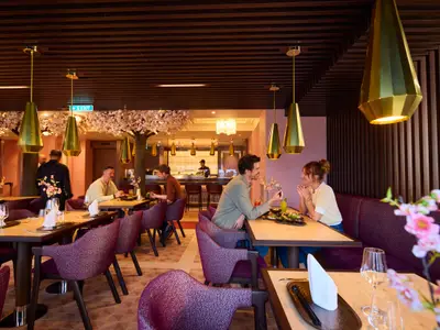 Ein Paar lacht sich an, während es in einem modern eingerichteten Asian-Restaurant an Bord der AIDAdiva speist. Im Hintergrund weitere Gäste und eine Sushi-Bar.