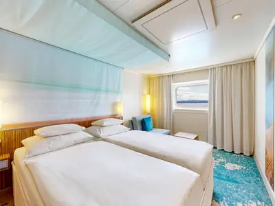 Eine geräumige Meerblickkabine an Bord der AIDAluna mit zwei gemütlichen Einzelbetten, maritimem Dekor und einem Fenster mit Blick auf das Meer und Berge.