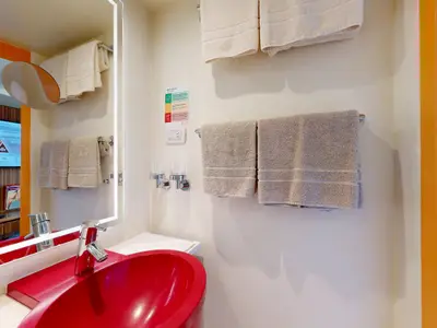 Das moderne Badezimmer einer Balkonkabine an Bord der AIDAluna mit einem leuchtend roten Waschbecken und einem großen, beleuchteten Spiegel.