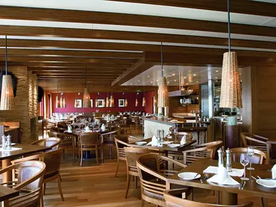 Innenansicht des Buffalo Steakhouse an Bord der AIDAluna. Elegante Holztische, rustikale Steinwände und geflochtene Hängelampen schaffen eine warme und gemuetliche Atmosphäre für Gäste.