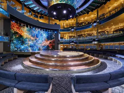 Das mehrstöckige Theatrium an Bord der AIDAnova, mit einer runden Bühne, umgeben von Sitzgelegenheiten, und einer riesigen LED-Wand, die eine Galaxie darstellt.