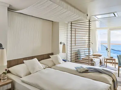 Moderne Balkonkabine an Bord der AIDAnova mit zwei Einzelbetten und einem Ausziehbett. Große Balkontüren bieten einen weiten Blick auf das offene Meer.