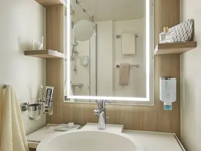 Modernes Badezimmer an Bord der AIDAnova. Es zeigt einen beleuchteten Spiegel, Waschbecken, Handtücher und Hygieneartikel. Die helle Einrichtung ist funktional.