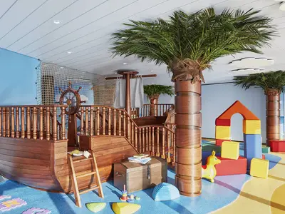Farbenfroher Kids Club an Bord der AIDAnova mit Holz-Piratenschiff, Steuerrad, Palmen und Softplay-Bloecken. Der Boden ist als Strand und Meer gestaltet. Ohne Personen.