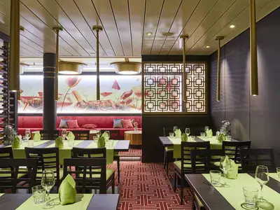Das East Restaurant der AIDAnova zeigt gedeckte Tische, rote Bänke und ein Wandbild mit Seerosen.