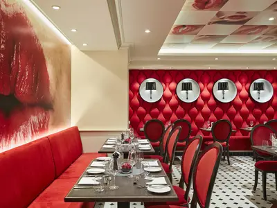 Das Restaurant 'French Kiss' der AIDAnova mit roten Sitzbänken, Samtstühlen und gedeckten Tischen. Auffällige rote, wellenförmige Wandpaneele und Deckenplatten mit Lippenmotiven.