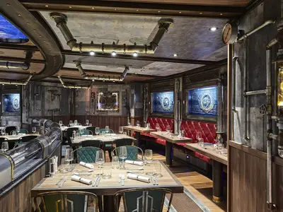 Innenansicht des "Time Machine" Restaurants an Bord der AIDAnova. Auffälliges Steampunk-Design mit Rohren, Zahnrädern, roten Lederbänken und dunklen Tischen, alle gedeckt.