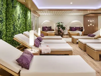 Entspannter Spa-Bereich an Bord der AIDAnova. Helle Rattan-Liegen mit lila Kissen und eine grosse grüne Pflanzenwand schaffen eine ruhige Atmosphäre.