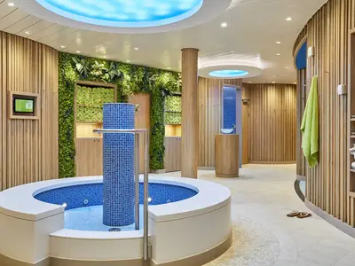 Der einladende Body & Soul Organic Spa an Bord der AIDAnova zeigt einen modernen Whirlpool mit blauen Mosaikfliesen und eine naturnahe Gestaltung mit Holzverkleidungen und Gruenpflanzen an den Waenden. Helle Handtuecher und Badeschuhe sind zu sehen.