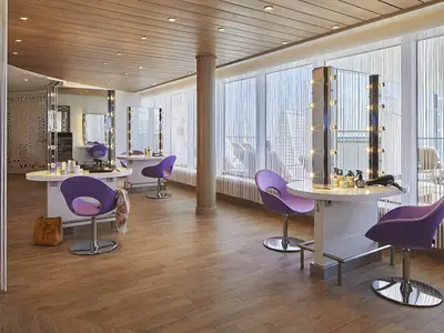 Heller Friseursalon an Bord der AIDAnova mit mehreren modernen Styling-Stationen, violetten Stühlen und großen Fenstern mit Blick nach draußen.