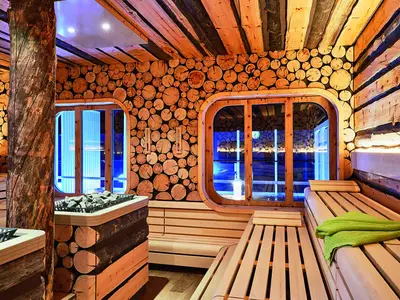 Geräumige finnische Sauna an Bord der AIDAnova mit Holzbänken und Wänden aus Baumstammscheiben. Blaue Lichter sind durch die Fenster sichtbar.