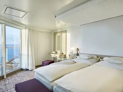 Einrichtung einer modernen Balkonkabine an Bord der AIDAnova mit zwei Einzelbetten und einem Schminktisch. Große Fensterfront mit Meerblick und Balkon mit Liege.
