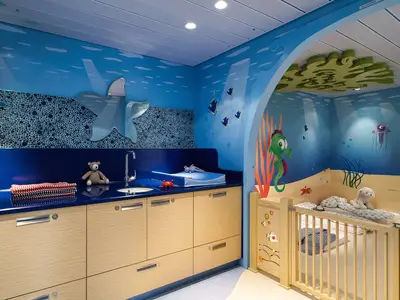 Der liebevoll gestaltete Mini Club an Bord der AIDAperla zeigt eine Unterwasserwelt mit hellblauen Wänden, Wickeltisch und Holzkrippen. Zahlreiche bunte Meeresmotive schmücken den Raum.