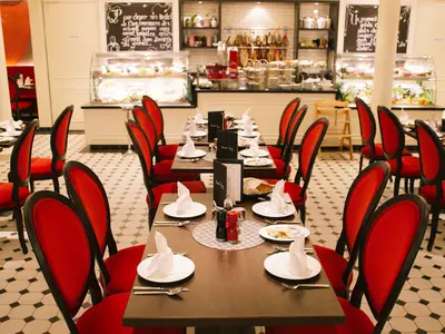 Blick in das elegant eingerichtete French Kiss Restaurant an Bord der AIDAperla mit zahlreichen gedeckten Tischen und markanten roten Stühlen. Im Hintergrund sind Auslagen mit Speisen zu sehen.