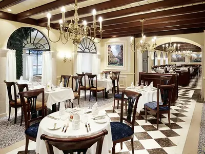 Elegantes Restaurant Casa Nova an Bord der AIDAperla mit dunklen Holzstühlen, weißen Tischdecken und goldenen Kronleuchtern. Im Hintergrund ein Bereich mit kariertem Boden.