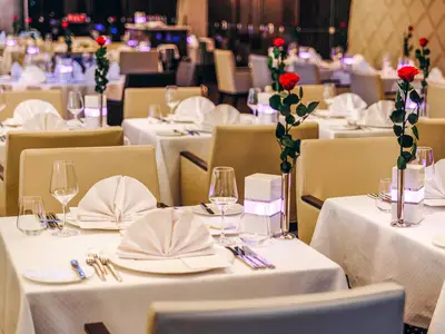 Elegantes Restaurant an Bord der AIDAperla. Festlich gedeckte Tische mit weißen Tischdecken, Gläsern, Besteck und roten Rosen in goldenen Vasen. Stilvolles Ambiente lädt ein.