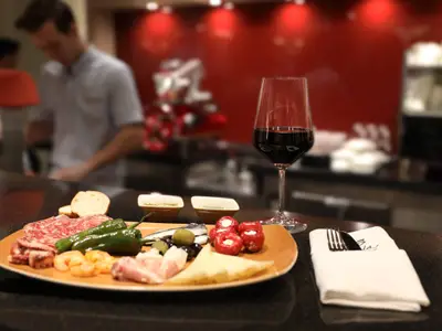 Eine appetitliche Tapas-Platte mit Wein, Oliven und verschiedenen Speisen auf einer Theke an Bord der AIDAperla. Im Hintergrund arbeitet unscharf ein Crewmitglied.