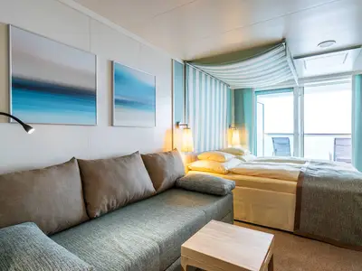 Eine helle und einladende Verandakabine Komfort an Bord der AIDAprima mit einem bequemen Doppelbett, einem Sofa und Zugang zu einem privaten Balkon mit Meerblick.