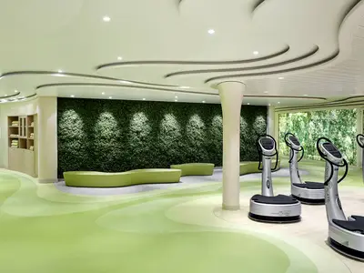 Ein heller Body & Soul Sport Bereich an Bord der AIDAprima. Die moderne Halle ist in hellgruenen Farbtönen gestaltet und mit Power Plate Geraeten sowie einer Wand aus Kunstpflanzen versehen.