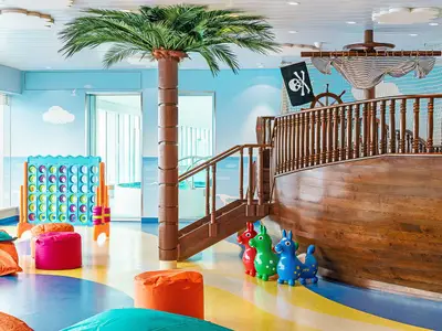Der farbenfrohe Kids Club an Bord der AIDAprima bietet ein Piratenschiff zum Klettern, ein riesiges Connect Four und bunte Hüpftiere für Kinder. Eine große Palme schmückt den Raum.