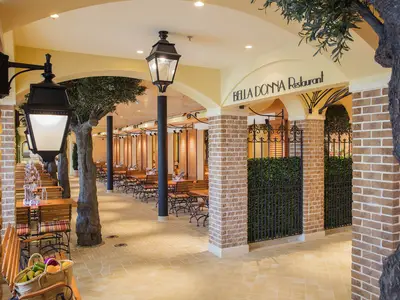 Helles, mediterranes Bella Donna Restaurant an Bord der AIDAprima. Zahlreiche Tische und Stühle unter Arkaden, mit künstlichen Olivenbäumen und Laternen.