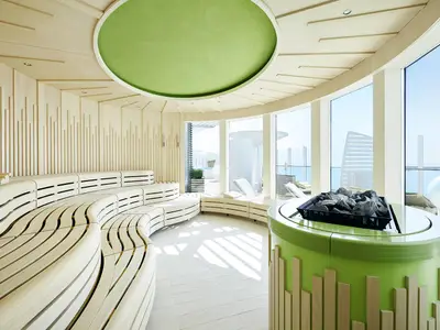 Moderne finnische Sauna an Bord der AIDAprima. Geschwungene Holzbankreihen und grüner Steinofen. Bodentiefe Fenster mit Meerblick. Helles Holz und grüne Decke.