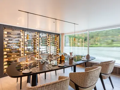 Panorama Restaurant: Elegantes Restaurant auf der AMADEUS Amara mit beleuchteter Weinwand und gedecktem Tisch. Große Fensterfront mit Blick auf grüne Flusslandschaft.