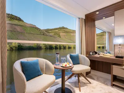 Moderne, helle Kabine auf dem Mozart and Strauss Deck der Amadeus Amara mit Panoramafenster. Blick auf Fluss und terrassierte Weinberge. Innen Sessel, Snacks und Schreibtisch.