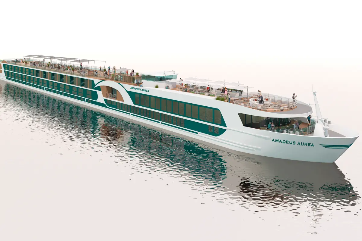 Eine Schrägansicht der Amadeus Aurea. Das Schiff ist weiß und türkisgrün, mit mehreren Decks und großen Fenstern. Zahlreiche Passagiere sind auf den offenen Decks und in den verglasten Lounges zu sehen. Die Wasseroberfläche spiegelt das Schiff leicht.