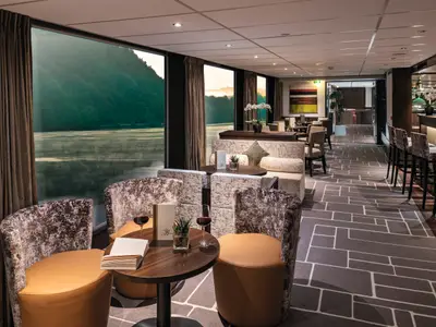 Eine elegante Schiffsbar mit gemusterten Sesseln, hellbraunen Ledersitzen und Holztischen. 