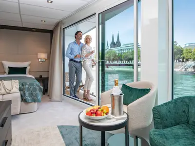 Ein Paar steht auf dem Balkon einer modernen Kabine der AMADEUS Cara mit Blick auf den Rhein und den Kölner Dom. 