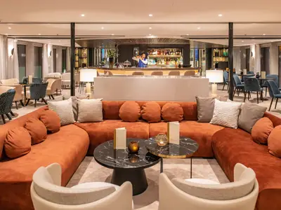 Eine elegant eingerichtete Bar-Lounge auf der AMADEUS Cara. Ein Barkeeper mixt Getraenke an einer langen Theke. 