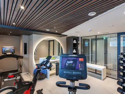 Ein helles und modernes Fitnessstudio auf der AMADEUS Cara. Mehrere Life Fitness Geräte, darunter Laufbänder, stationäre Fahrräder und ein Hantelständer, sind zu sehen. Eine große runde Spiegelfläche und Holzakzente an der Decke prägen den Raum.