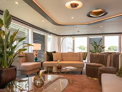 Eine helle und luxuriöse Lounge auf der AMADEUS Cara mit modernen Sofas, Sesseln, Pflanzen und grossen Fenstern mit Blick nach draussen.