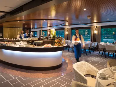 Buffetrestaurant auf der AMADEUS Diamond. Moderne Theke mit Speisen und Früchten, gedeckte Tische und Crew. 