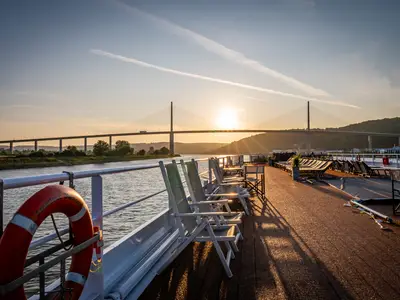 Blick vom sonnenbeschienenen Sonnendeck der AMADEUS Diamond bei Sonnenuntergang. Imposante Brücke über dem Fluss im Hintergrund.