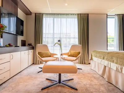 Helle Suite auf der AMADEUS Diamond mit Doppelbett, zwei Sesseln, Ottoman, und einem Fenster mit Blick auf die Stadt.