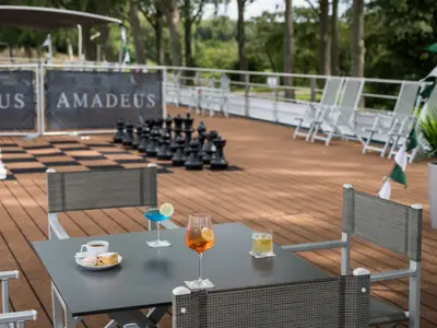 Blick auf das Sonnendeck der AMADEUS Imperial mit einem riesigen Schachbrett. Im Vordergrund stehen Tische mit Getraenken und einem Gebaeck. 