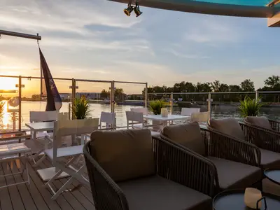 Panoramablick auf das Sonnendeck der AMADEUS Imperial bei Sonnenuntergang. Bequeme Lounge-Sessel, Tische mit Kerzen und Stühle stehen bereit. 