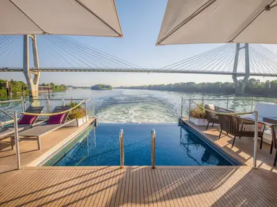 Blick vom Heck der AMADEUS Provence. Ein Infinity-Pool führt ins glitzernde Wasser. Links und rechts laden Sonnenliegen und Loungesessel zum Entspannen ein. 